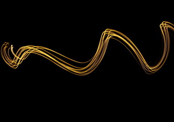 Long exposure photograph of neon gold colour in an abstract swirl, parallel lines pattern against a black background. Light painting photography.