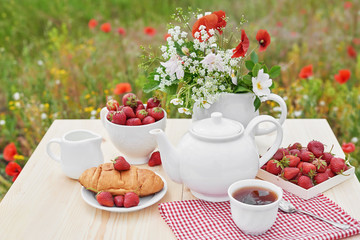 Romantic Valentines french or rural breakfast: tea, strawberries, croissants on table in poppy field. Countryside and Cozy Good morning weekend concept. Background with copy space. Date outdoors