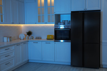 Fototapeta premium Stylish kitchen interior with modern refrigerator at night