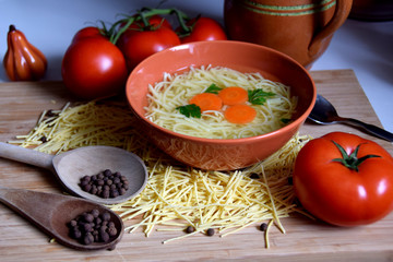 delicate chicken broth in a bowl next to tomatoes, spices and kitchen utensils