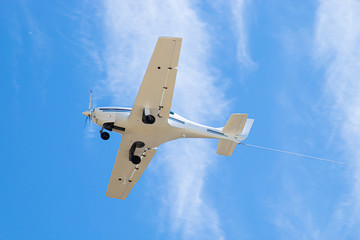 airplane in a blue sky with clouds pulls a rope © Denis