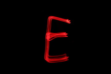 Long exposure photograph of the letter e in neon red colour fairy lights against a black...