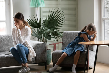 Fototapeta premium Offended young mother and small daughter sit separately back to back avoid talking after family fight, hurt mom and little girl child ignore each other after quarrel, generation gap concept