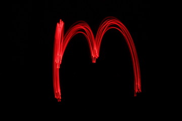 Long exposure photograph of the letter m in neon red colour fairy lights against a black...