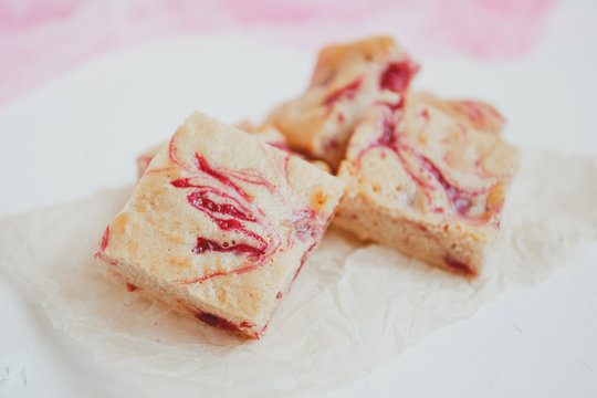 Homemade blondies, made of white chocolate with fresh raspberries, on a light background.