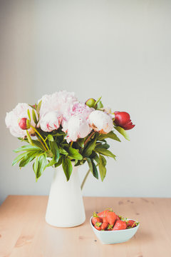 Toned photo Bunch of Pink peonies in vase and strawberry on the wooden table Flowers on a beige wooden table near the window. Home house interior. Beautiful peony flower.Summer day. Spring. Copy space