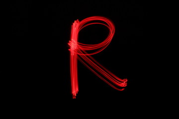 Long exposure photograph of the letter r in neon red colour fairy lights against a black...