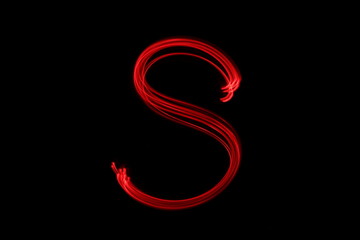 Long exposure photograph of the letter s in neon red colour fairy lights against a black...