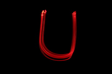 Long exposure photograph of the letter u in neon red colour fairy lights against a black background. Light painting photography. Part of an alphabet series. 
