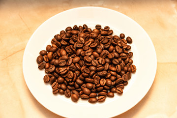 Roasted coffee grains lie on a white plate. Making a coffee drink.