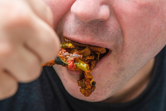 A man sends fried meat with sauce from a fork to his mouth, closeup.
