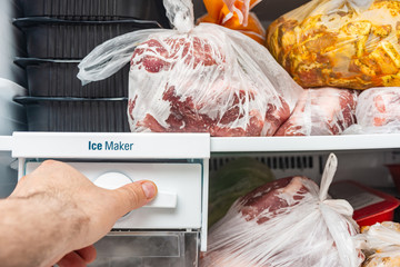A man opens a freezer with frozen food to switch the ice maker.