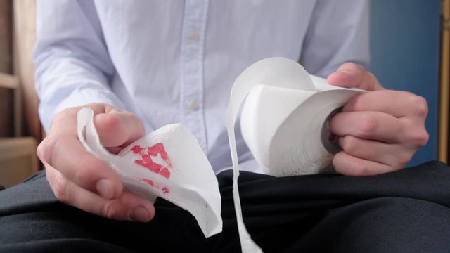 A man squeezes toilet paper in his hands, experiencing pain from hemorrhoids