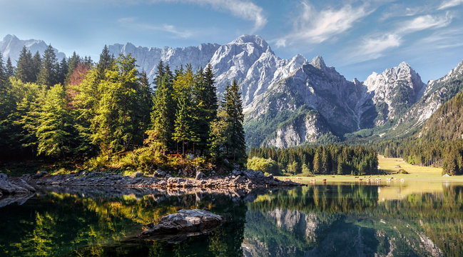 Impressive Autumn landscape during sunset. The Fusine Lake in front of the Mongart under sunlight. Amazing sunny day on the mountain lake. concept of an ideal resting place. Creative image. © jenyateua