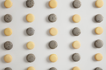Above shot of yellow lemon and grey macaroons arranged in rows against white background. Tasty cookies, traditional french macarons. Junk food, calories and nutrition concept. Confectionery.