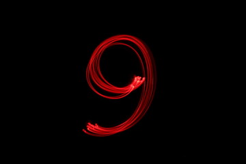 Long exposure photograph of the number 9 in neon red colour fairy lights against a black...