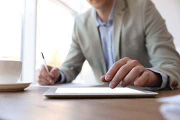 Businessman working with modern tablet at wooden table in office, closeup