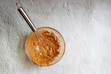 Whisking melted chocolate with cream; stain in a glass mixing bowl on table background. 