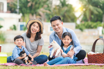 An Asian family plays with a Shiba Inu dog. Family has father, mother and son, daughter. Picnicking in the garden.