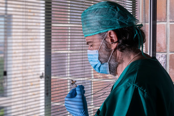 Mature doctor, with a beard and mask, prays before a crucifix