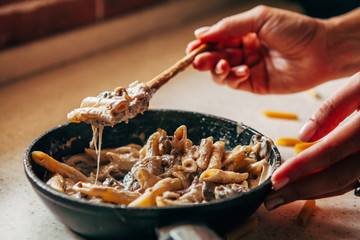 A female hand takes a spoon with pasta from a skillet