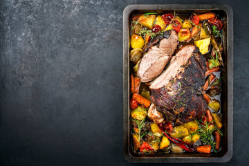 Traditioneller gegrillter Lammbraten aufgeschnitten mit Tomaten und Bratkartoffel als Draufsicht auf einem Tablett mit Textfreiraum links