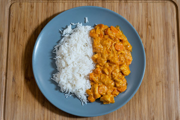 Plate of white rice with chicken and curry sauce on a wooden table.