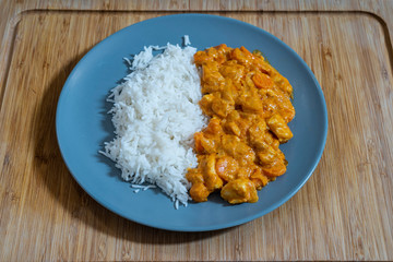 Plate of white rice with chicken and curry sauce on a wooden table.