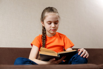 Little girl reading a book on the sofa. Caucasian little girl spending alone time relaxing on the couch with an old book.