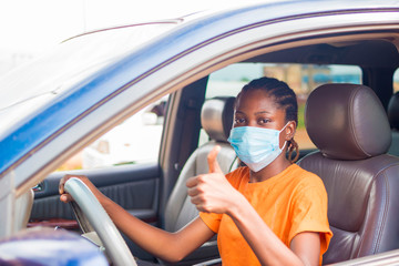 young beautiful african lady in a vehicle wearing face mask to prevent, preventing, prevented herself from the outbreak in the society and did thumbs up