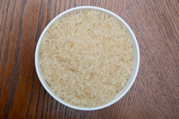 White rice in a white Cup on a brown table.