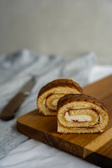 Two slices of sponge cake roll are laying on a wooden cutting board against background of knife
