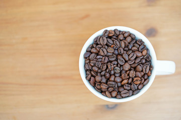 Coffee beans in a cup on wooden background
