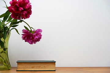 Still life with pink peony flowers and closed old book.