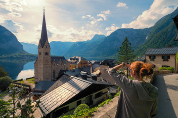 Female tourist looking at stunning Hallstatt, Salzkammergut region, OÖ, Austria, from an elevated viewing point above the roofs of the famous village