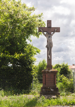 Krucyfiks przy drodze. Wiara katolicka. Pomnik w Niemczech.  Miasto w Hesji. Mala architekura. Kamienny pomnik.  Krzyz pod pochmurnym niebem. Szare i ciezkie chmury.