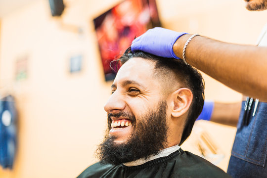bearded man smiling while getting his hair done at the barbershop