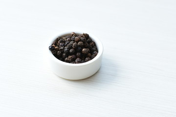 Fototapeta na wymiar Black peppercorns in bowls on white wooden background