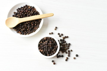 Black peppercorns in bowls on white wooden background