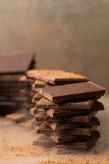 Pieces of dark chocolate bars against a background of cocoa powder and smoke. Vertical format, space for text