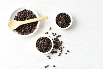 Black peppercorns in bowls on white wooden background