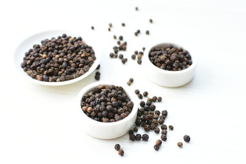 Black peppercorns in bowls on white wooden background
