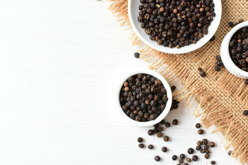 Black peppercorns in bowls on white wooden background
