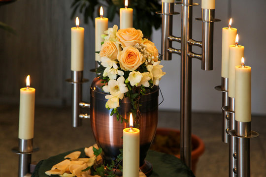 Urne mit Rosen und Kerzen verziert in einer Friedhofskapelle kurz vor einer Bestattung.