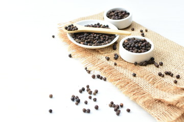 Black peppercorns in bowls on white wooden background