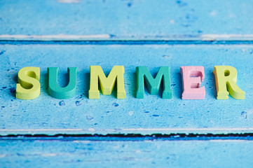 the word summer laid with colored wooden letters on blue background with copy space