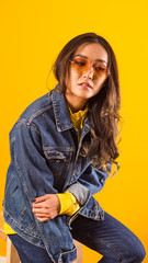 A girl of Asian appearance in a jeans stomatitis on a yellow background, in yellow glasses and wavy hair, business spoils