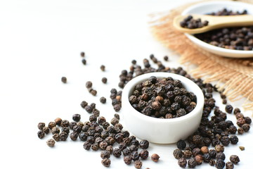 Black peppercorns in bowls on white wooden background
