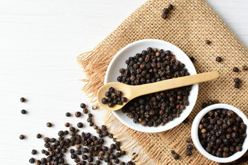 Black peppercorns in bowls on white wooden background