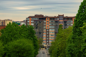 Eastern Europe green street trees foliage go to vintage style living building architecture facade of red and brown color in cloudy gray summer day